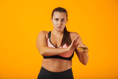 Görüntü izole sarı arka plan üzerinde sandviç tutarak dur jest yapıyor eşofman içinde ciddi tombul kadın