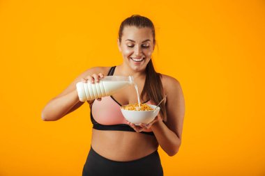 Görüntü üzerinde sarı arka plan izole kahvaltı için süt ve Mısır gevreği tutan eşofman genç kilolu kadının