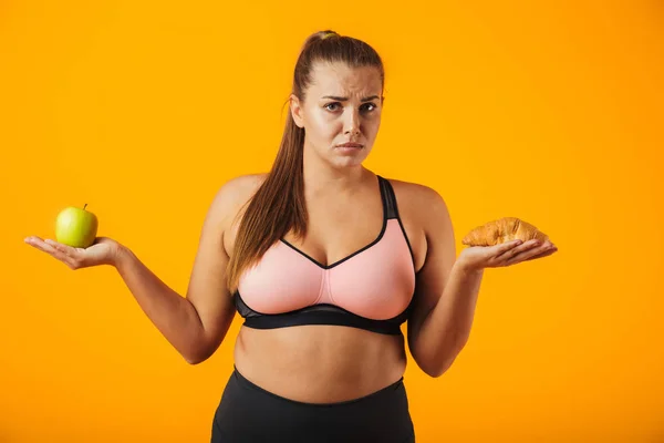 Image Puzzled Chubby Woman Tracksuit Holding Apple Croissant Both Hands — Stock Photo, Image