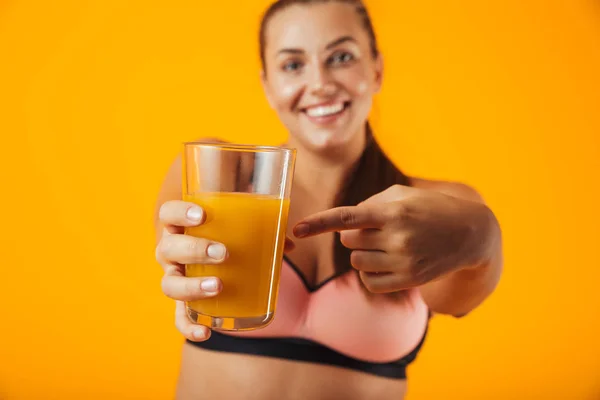 笑みを浮かべて 黄色背景に分離したオレンジ ジュースのガラスを保持トラック スーツで素敵なぽっちゃり女性の画像 — ストック写真