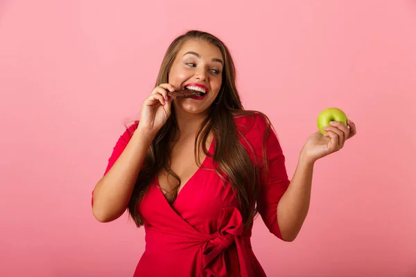 一个快乐的年轻女子的形象隔离在粉红色的墙壁背景举行巧克力和苹果 — 图库照片