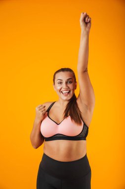 Gülümseyen ve sarı arka plan üzerinde izole ayakta sportif sütyen genç tombul kadın portresi