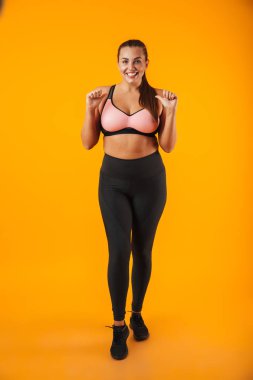 Tam uzunlukta sarı arka plan üzerinde izole ayakta giyim spor giyen bir neşeli kilolu fitness kadın portresi