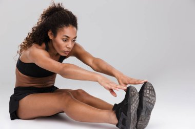 Genç ve güzel bir Afrika sporcumuz gri arka plan üzerinde izole germe egzersizleri yapıyor portresi