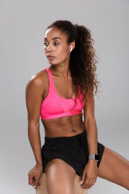 Süre oturan ve kulaklık ile müzik dinlemek dinlenme gri arka plan üzerinde yorgun genç Afrika sporcumuz portresi tam uzunlukta izole