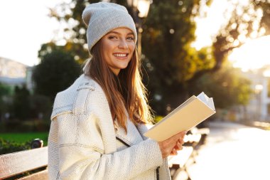 Görüntü okuma kitabı açık havada tutan bankta oturan bir kızıl saçlı kadın.
