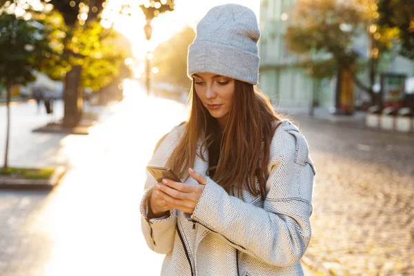 屋外身に着けている帽子は 携帯電話のチャットを歩く美しい赤毛の女性のイメージ — ストック写真