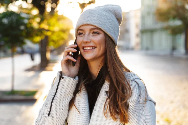 屋外身に着けている帽子は 携帯電話での話を歩く美しい赤毛の陽気な女性のイメージ — ストック写真