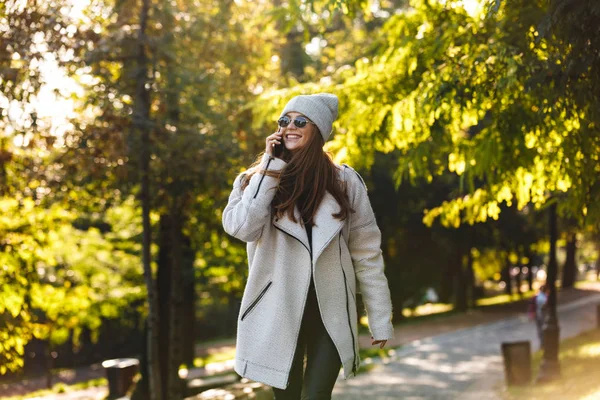 美丽的年轻女子穿着秋外套和帽子走在户外 在手机上交谈 — 图库照片