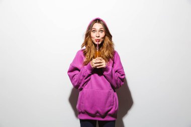 Neşeli kadın 20'li yaşlarda giyen kazak beyaz arka plan üzerinde izole saman kullanarak soda içme portresi