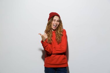 Başparmak gösterilmesini beyaz arka plan üzerinde izole ayakta kapüşonlu neşeli genç bir kadın portresi