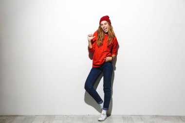 Beyaz arka plan üzerinde duran, parmak işaret kapüşonlu genç mutlu bir kadın portresi tam uzunlukta