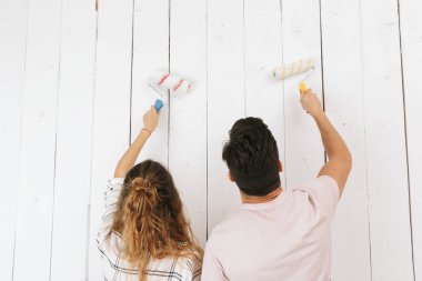 Mutlu çift adam ve beyaz duvar boyama ve boya merdaneleri kullanarak yenileme yapma kadın fotoğrafı