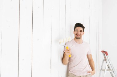 Görüntü yenileme boya silindiri kullanarak neşeli adam 20'li yaşlarda resim beyaz duvar ve yapımı