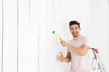 Görüntü yenileme boya silindiri kullanarak mutlu erkek 20'li yaşlarda resim beyaz duvar ve yapımı