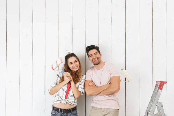 Photo of smiling couple man and woman painting white wall and making renovation using paint rollers