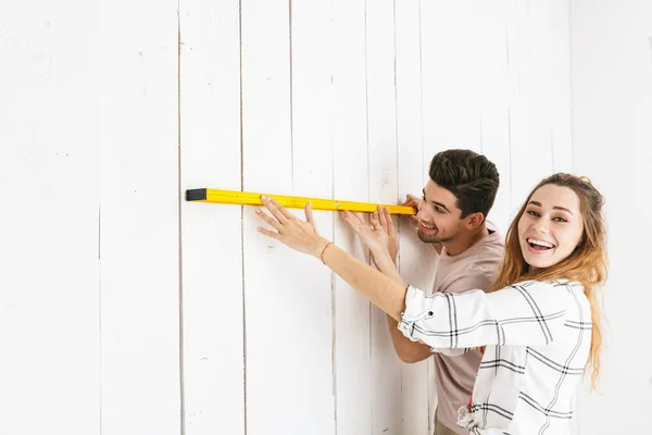 魅力的なカップル男性と女性持株大きな定規で測定し 屋内改修中の白い壁の写真 — ストック写真