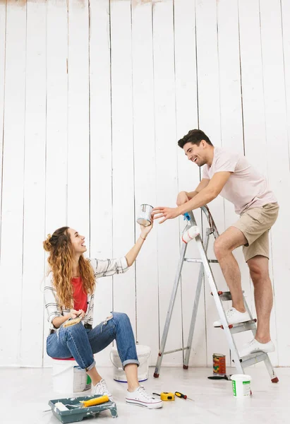 Photo of attractive couple man and woman using ladder while painting wall and making renovation indoor