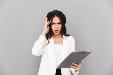 Karışık bir genç kadının portresi ceket ayakta tablet holding, gri arka plan giymiş.