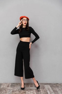 Genç ve güzel bir kadın portresi tam uzunlukta siyah pantolon ve gri arka plan üzerinde duran, uzakta seyir şapka giymiş