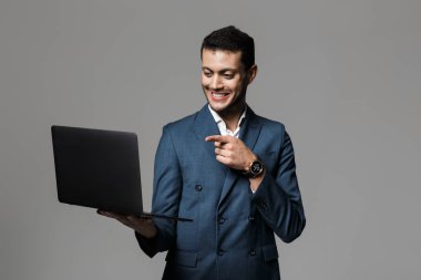 Görüntü gülümseyen ve gri arka plan üzerinde izole dizüstü holding resmi kıyafetli neşeli Arap adamın 30'lu