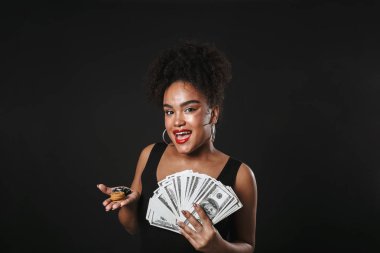 Güzel bir Afrikalı kadının poz görüntü para ve cips tutarak siyah duvardan izole.