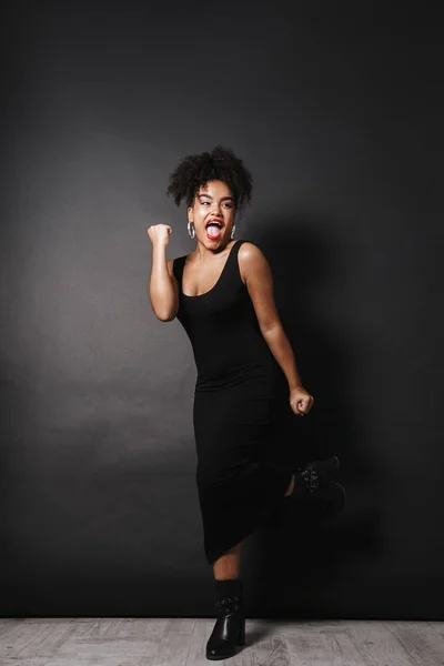 Full length photo of gorgeous afro american woman wearing black dress standing isolated over dark background