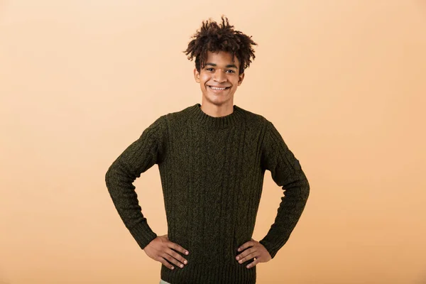 Portrait of a happy young africa man dressed in sweater isolated over beige background, standing with arms on hips