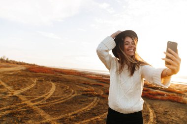 Bir selfie alarak sahilde günbatımı sırasında açık havada yürüyüş güzel gülümseyen genç kadın