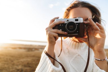 Sahilde günbatımı, fotoğraf çekimi sırasında fotoğraf makinesi ile açık havada yürüyen güzel genç kadın
