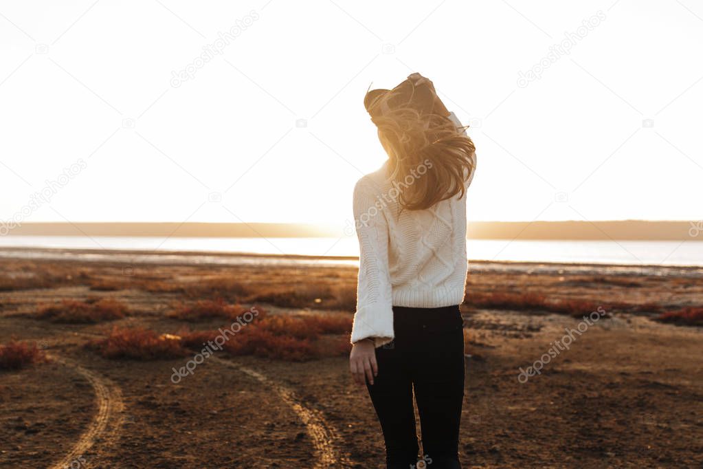 Back view of a beautiful young woman walking outdoors at the beach during sunset