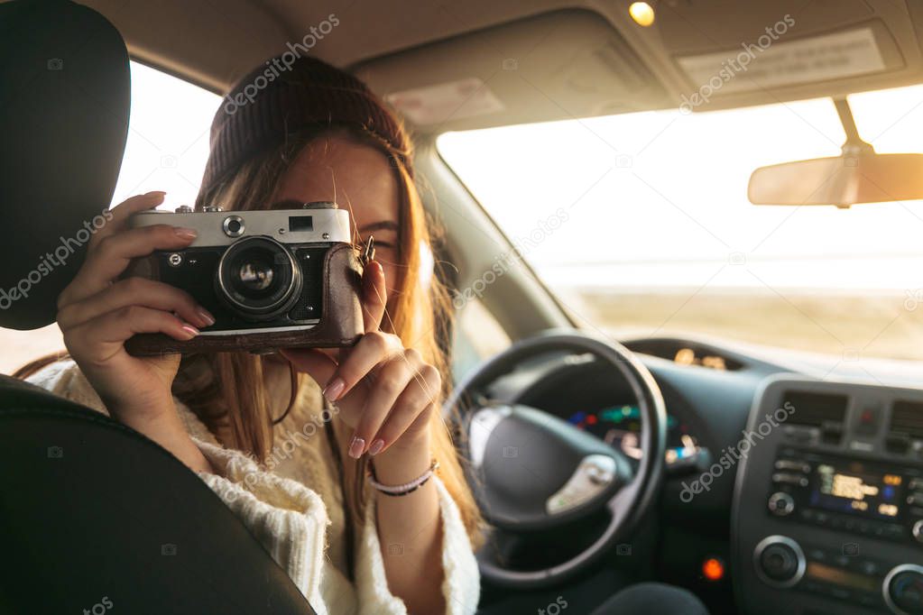 Woman taking a picture with photo camera while sitting on a drivers seat inside a car