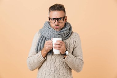 Kazak ve sıcak çay bej renkli arka plan üzerinde izole tutan eşarp portre Eğer gözlük donmuş bir adam giymiş