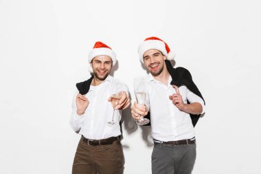 Two cheerful smartly dressed men standing isolated over white background, celebrating New Year, drinking champagne clipart