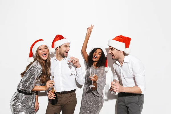 Group of four cheerful smartly dressed friends standing isolated over white background, celebrating New Year, drinking champagne