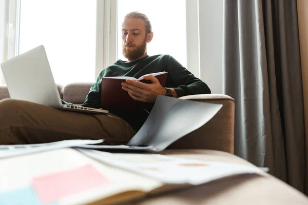 Knappe Jongeman Thuiswerken Zittend Een Bank Met Behulp Van Laptopcomputer — Stockfoto