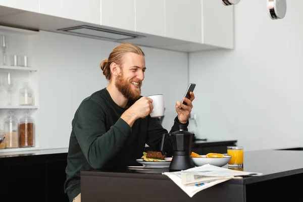 Handsome Young Man Having Breakfast Reading Newspaper While Sitting Kitchen — Stock Photo, Image