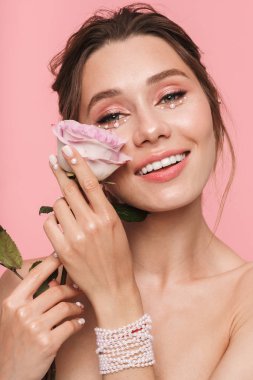 Beyaz inci giymiş pembe arka plan üzerinde izole bir çiçek ile poz çekici bir genç üstsüz kadın güzellik portresi