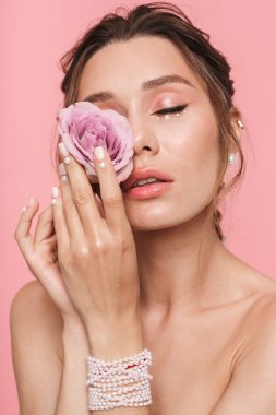 Beyaz inci giymiş pembe arka plan üzerinde izole bir çiçek ile poz çekici bir genç üstsüz kadın güzellik portresi