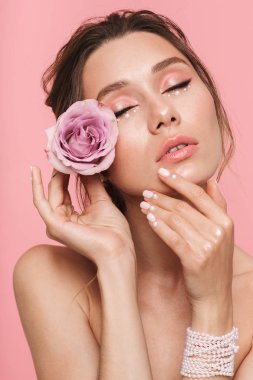 Beyaz inci giymiş pembe arka plan üzerinde izole bir çiçek ile poz çekici bir genç üstsüz kadın güzellik portresi
