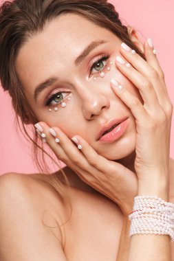 Güzellik kapatın beyaz inci bilezik takan pembe arka plan üzerinde izole poz çekici bir genç üstsüz kadın portresi