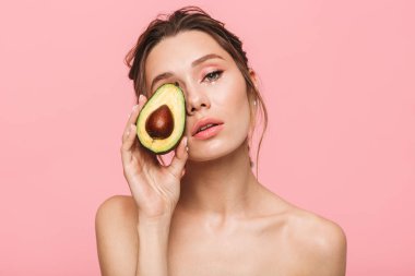 Beyaz inci giymiş pembe arka plan üzerinde bir avokado ile poz çekici bir sağlıklı genç üstsüz kadın portresi güzellik izole