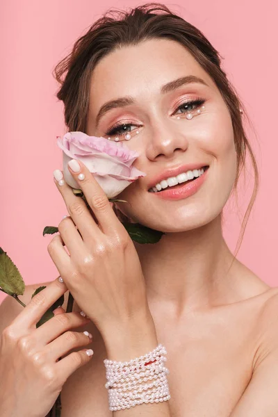 Beyaz inci giymiş pembe arka plan üzerinde izole bir çiçek ile poz çekici bir genç üstsüz kadın güzellik portresi