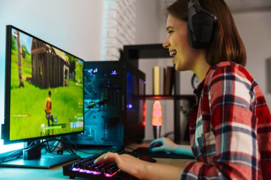 Bilgisayar oyunları oynarken masada oturan kulaklıklar giyen bir heyecanlı genç kadın portresi