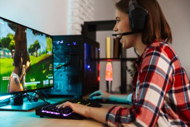 Bilgisayar oyunları oynarken masada oturan kulaklıklar giyen bir heyecanlı genç kadın portresi