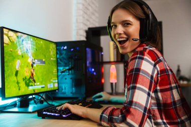 Bilgisayar oyunları oynarken masada oturan kulaklıklar giyen bir heyecanlı genç kadın portresi