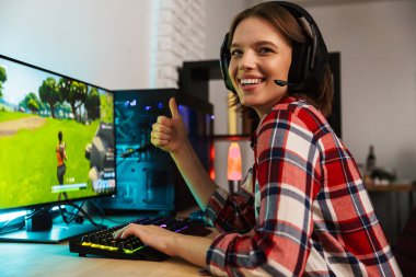 Bilgisayar oyunları oynarken masada oturan kulaklıklar giyen bir heyecanlı genç kadın portresi