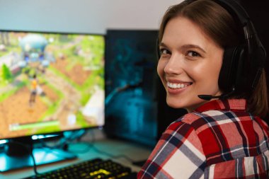 Bilgisayar oyunları oynarken masada oturan kulaklıklar giyen bir heyecanlı genç kadın portresi