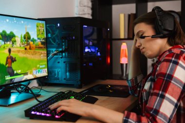 Bilgisayar oyunları oynarken masada oturan kulaklıklar giyen genç bir kadın portresi