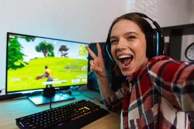 Bilgisayar çevrimiçi bir selfie alarak oyun, masada oturan kulaklıklar giyen bir heyecanlı genç kadın portresi